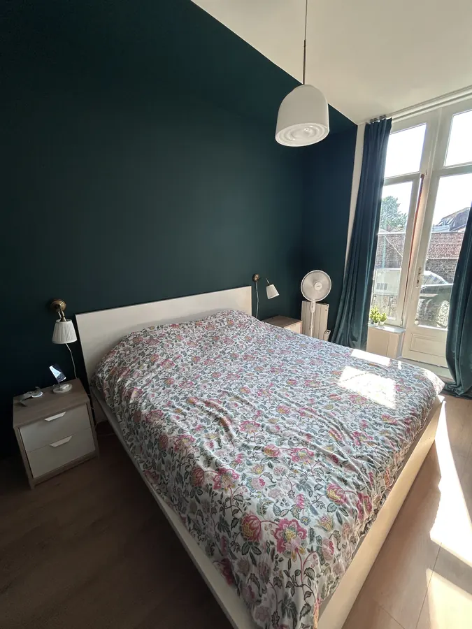 Chambre avec mur vert foncé, lit double et fenêtre côté cour