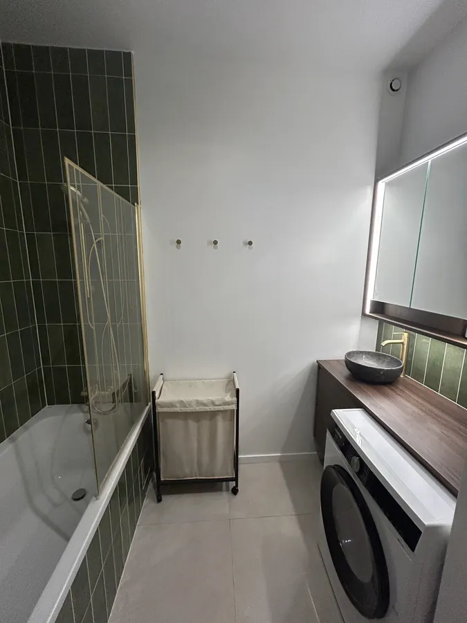 Salle de bain refaite à neuf avec faïence verte, baignoire et emplacement machine à laver